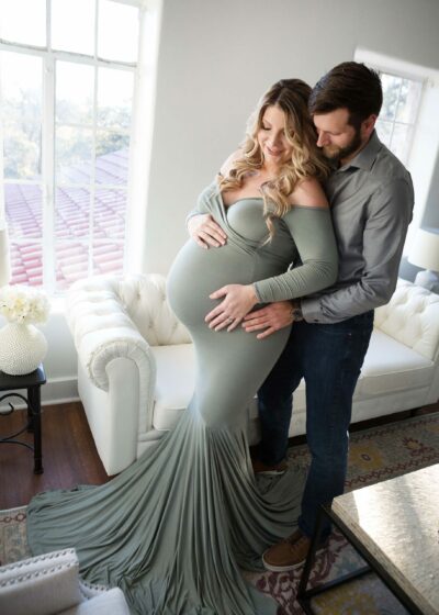 A pregnant woman and her husband are posing in front of a couch.