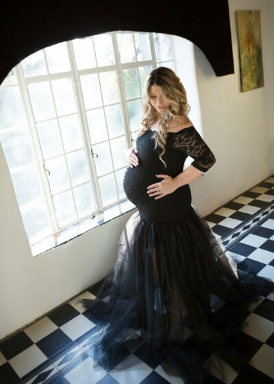 A pregnant woman in a black gown standing in a room.