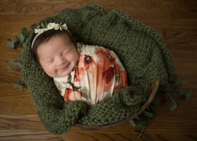 A baby girl is wrapped in a green blanket on a wooden floor.