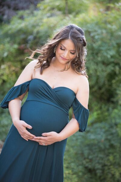 A pregnant woman in a teal dress is posing for a photo.