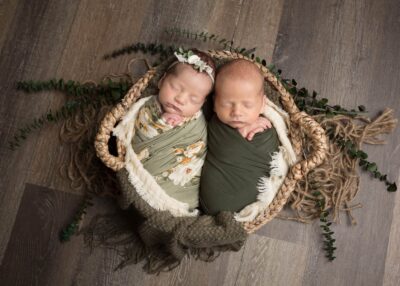 Two newborn twins in a basket on a wooden floor.