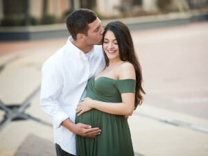 A pregnant couple kissing in front of a brick wall.