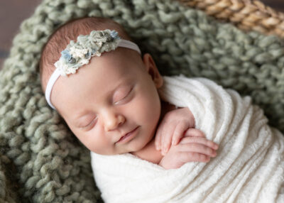 newborn baby girl smiling and wrapped in cream with during her photo shoot with jenn brookover photography in San Antonio, Tx